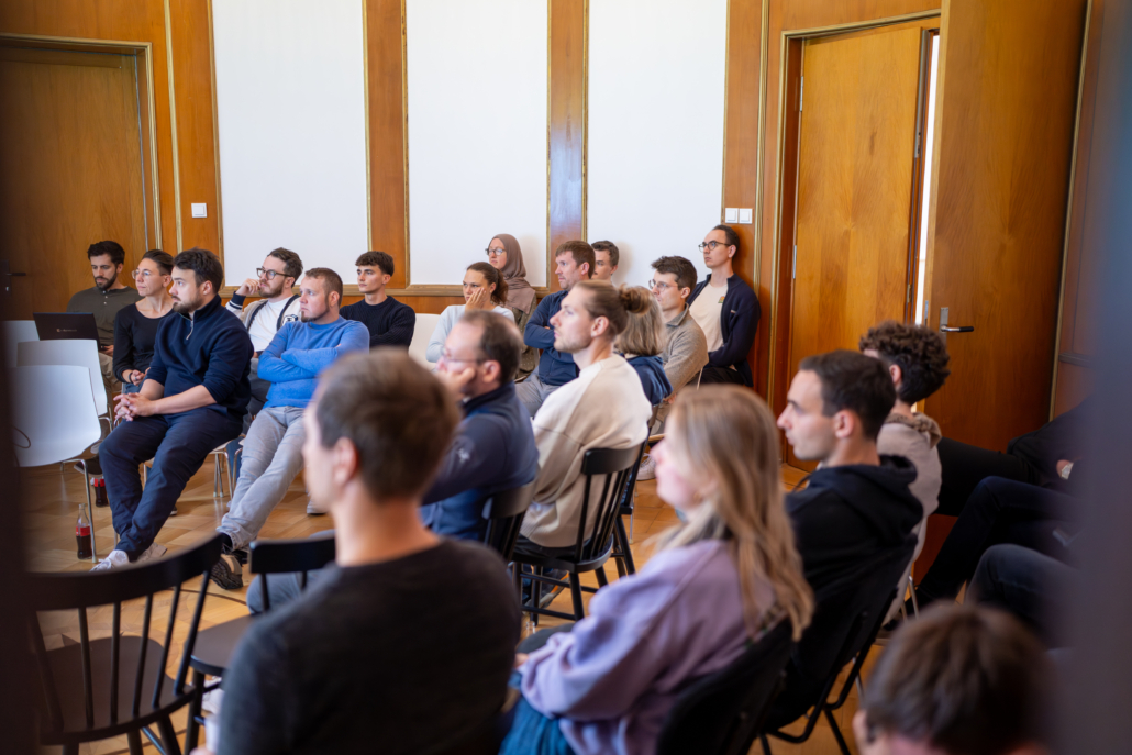 People sitting on chairs in a room with wood paneling and white walls, some facing forward.