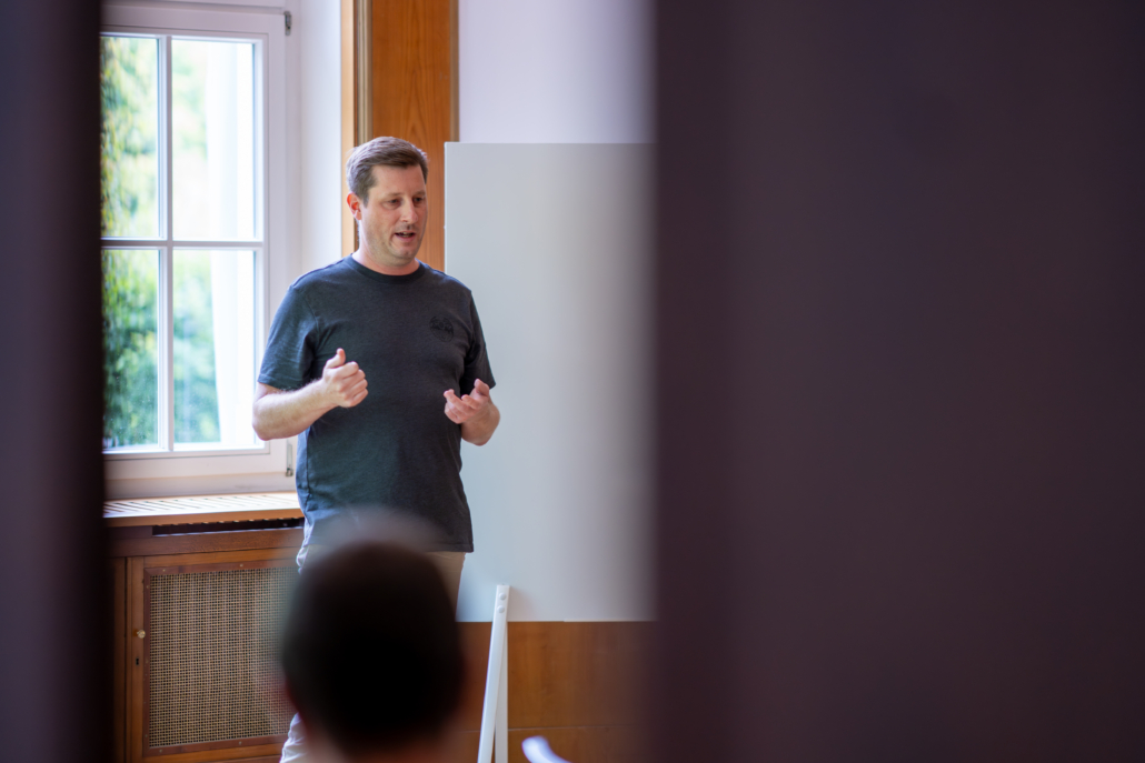 Person in schwarzem T-Shirt steht vor einem Fenster und einer weißen Tafel in einem Raum.